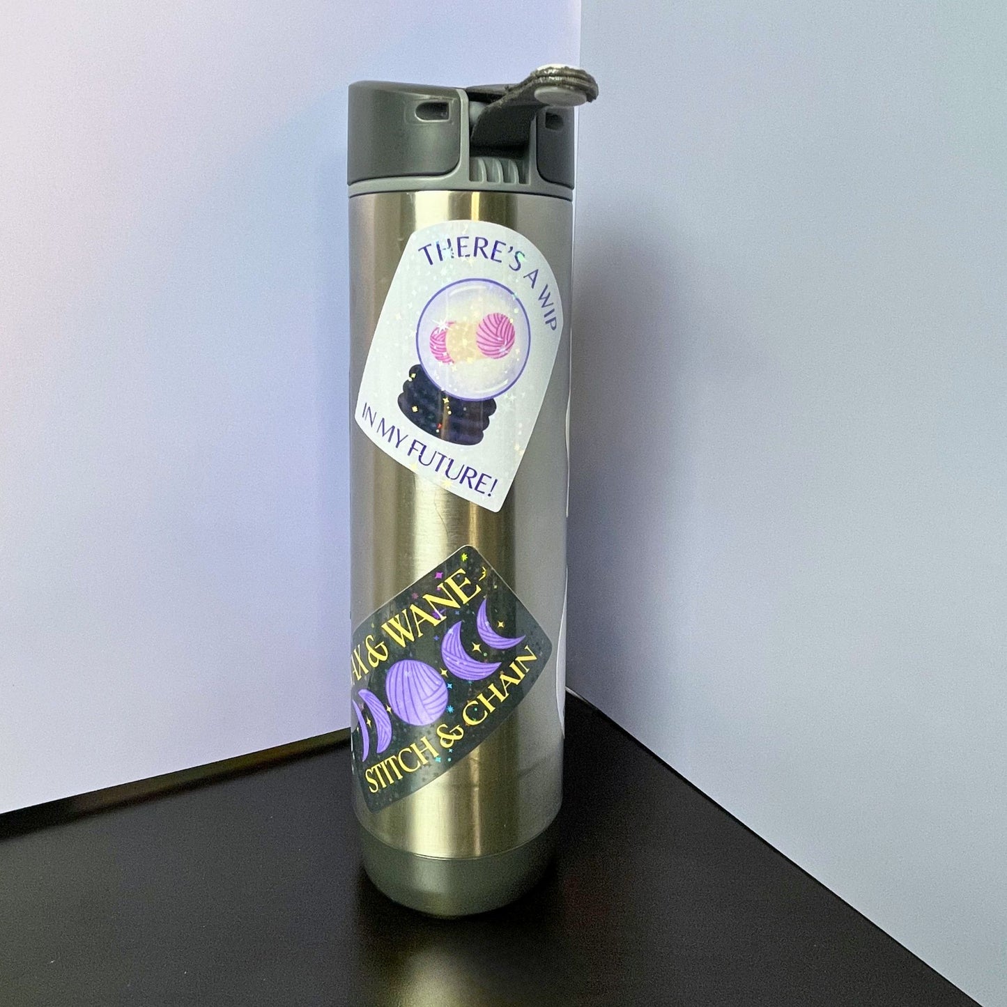 Silver water bottle with a label on a black surface against a white background