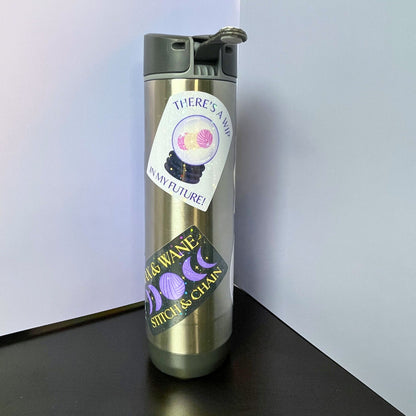 Silver water bottle with a label on a black surface against a white background